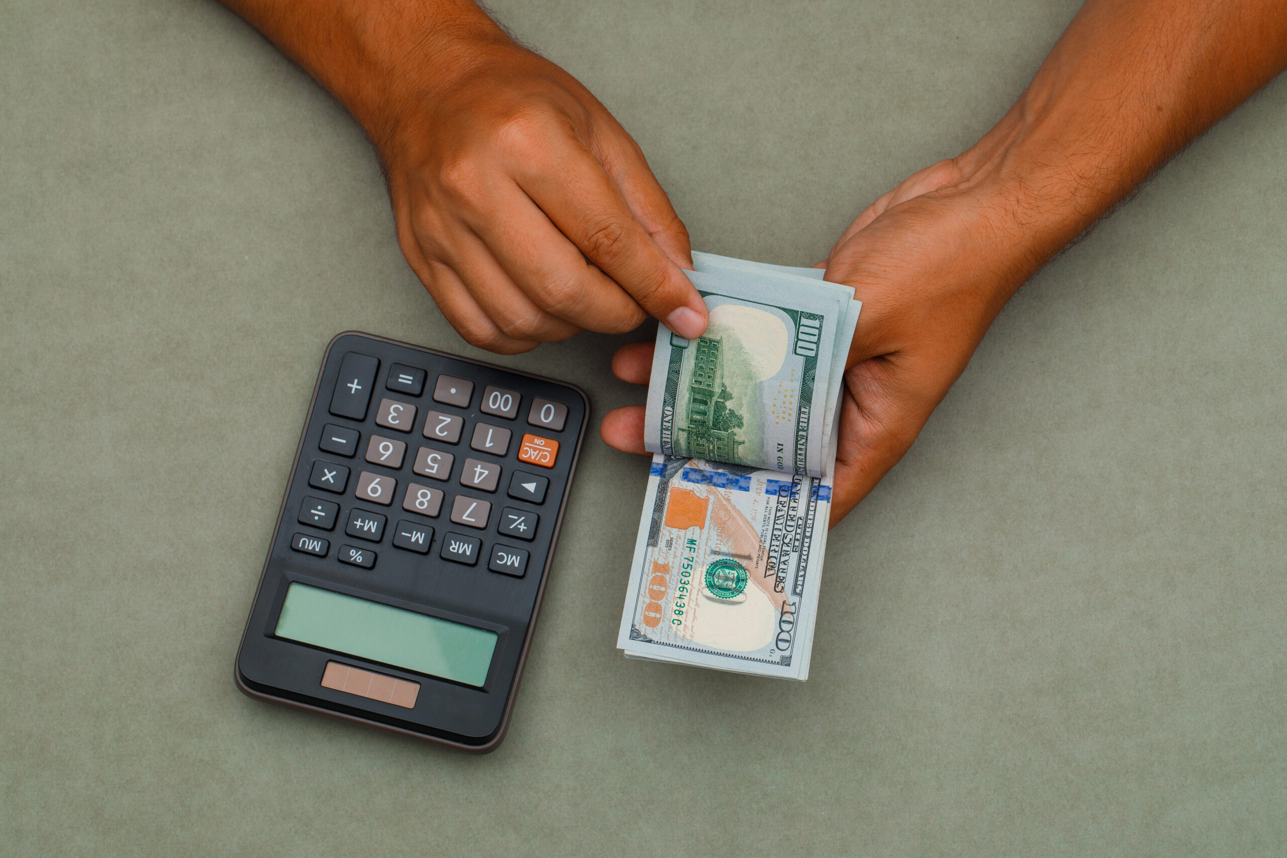 Accounting concept with calculator on green grey background flat lay. man counting dollar bills.