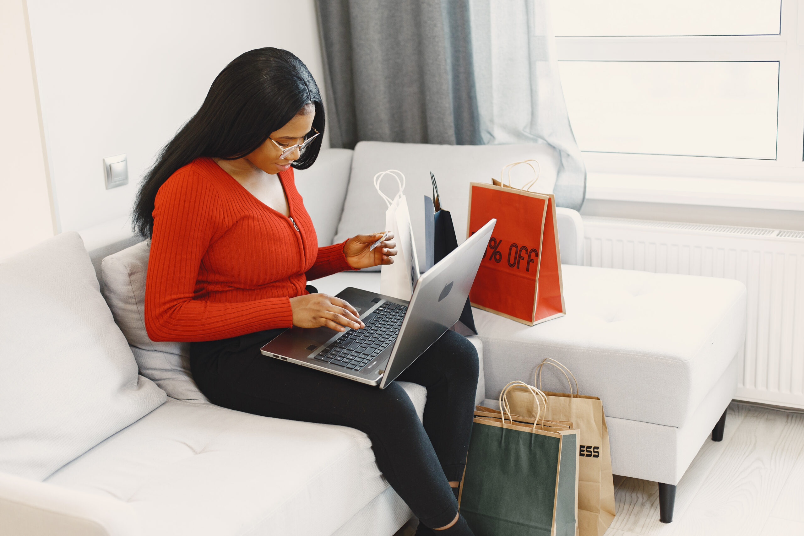Woman using computer and credit card. Bags near sofa. Lady in a red sweater.