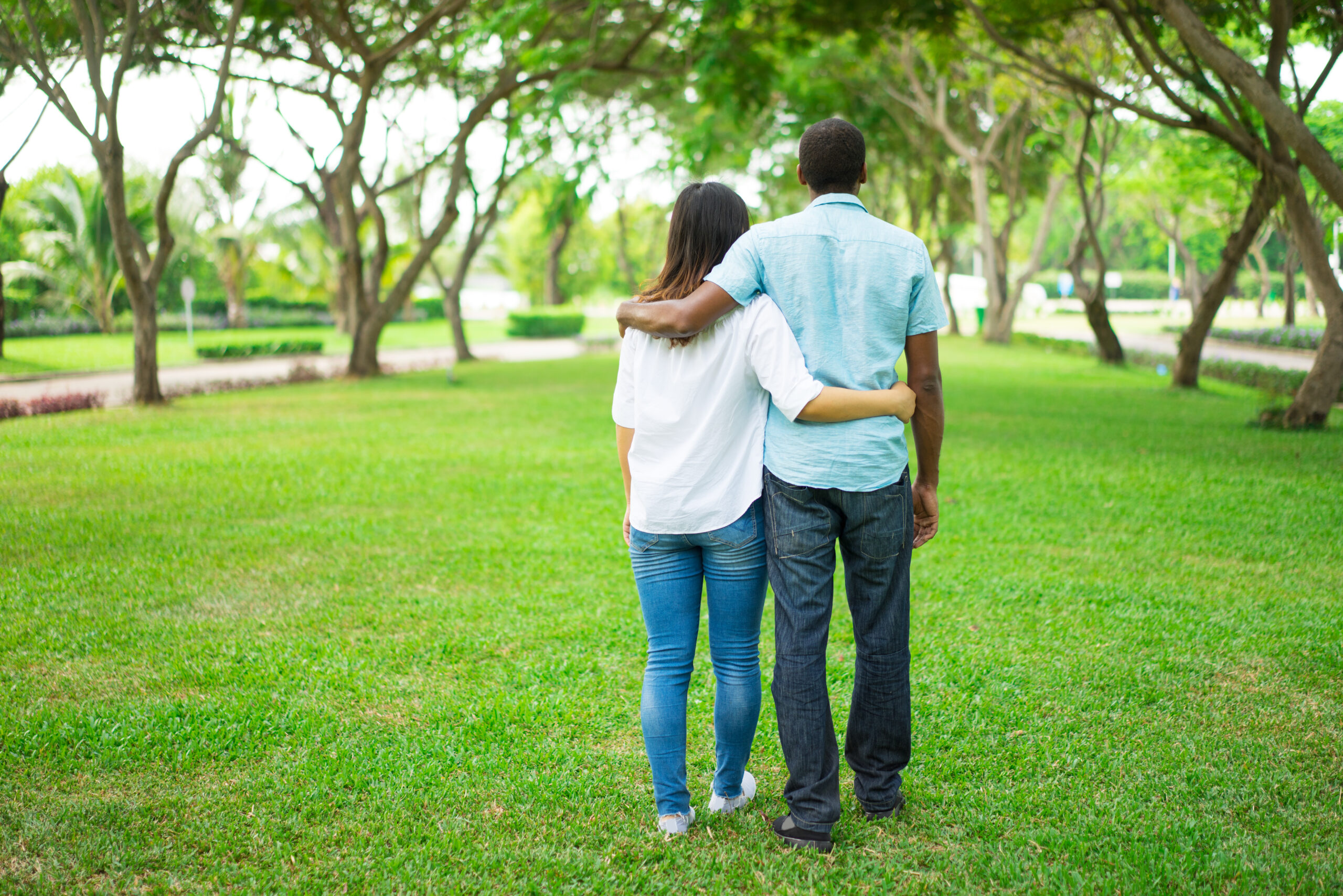 Rear view of young multiethnic couple embracing and walking in park. Caucasian woman and African American man walking in summer. Romance concept