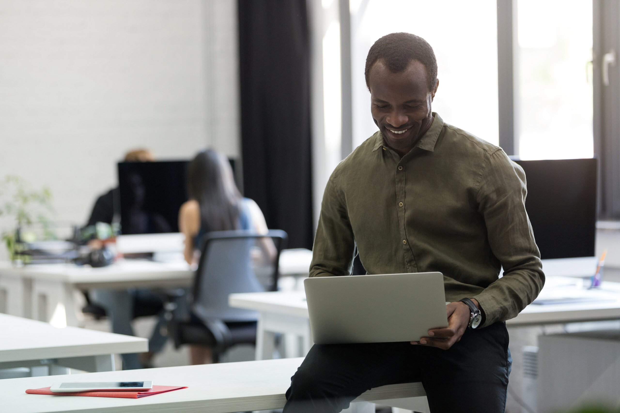 Happy afro american businessman sitting on his desk and typing on laptop computer in an office